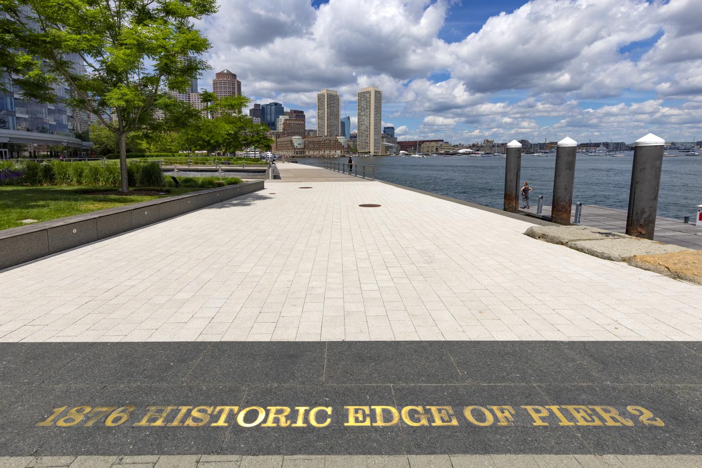 Waterfront promenade with city skyline and fluffy clouds.