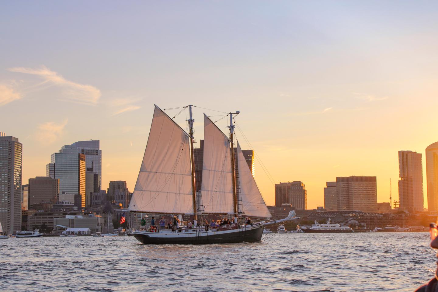 Sailboat on water at sunset, city skyline in background.